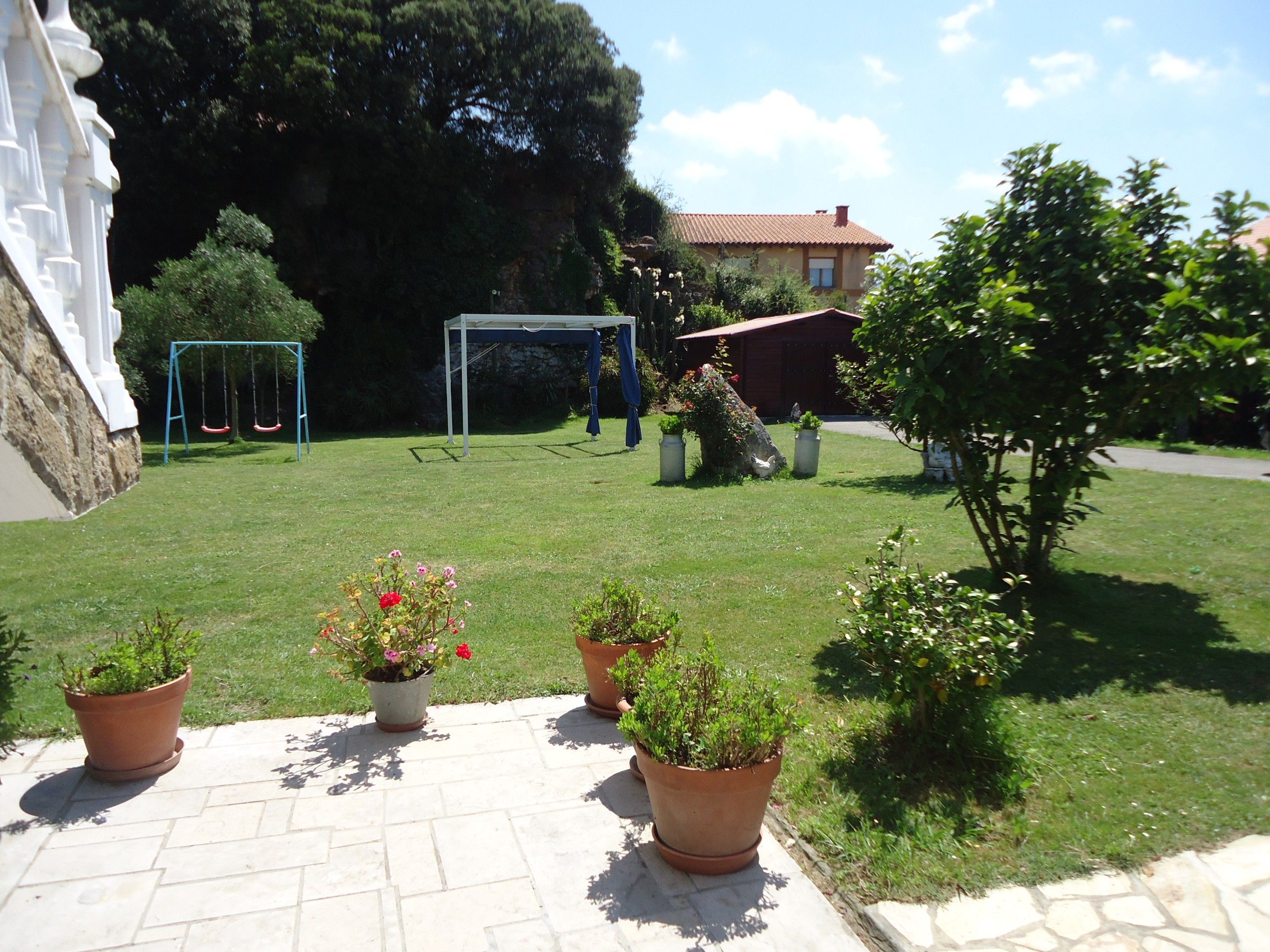 A courtyard with a swing set, a gazebo, potted plants, and a stone wall.