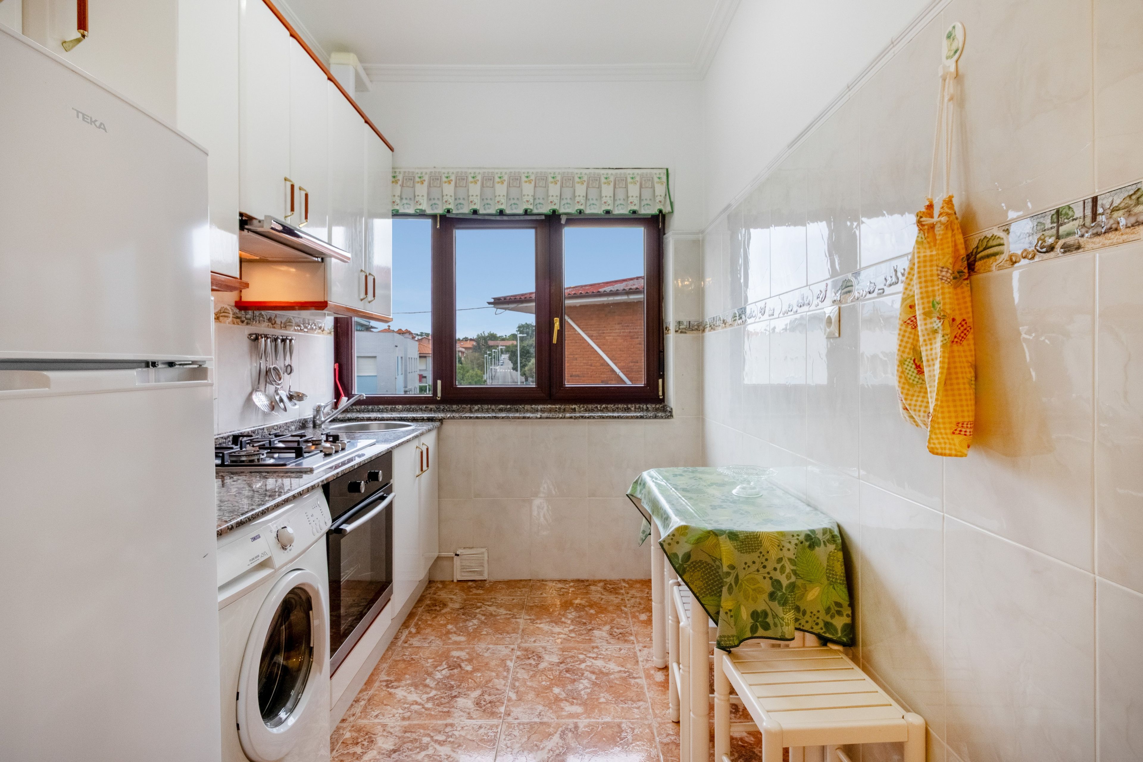 A compact kitchen with a washing machine, a sink, and a window with a view of the outside.