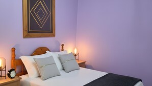 Ein Schlafzimmer mit Bett, Nachttischen, einer Chandelüster, einem gerahmten Kunstwerk und einem Beistelltisch mit Lampe.
