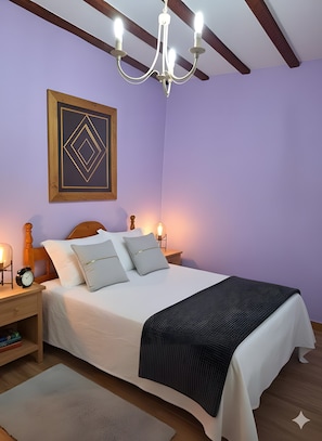 A bedroom with a bed, bedside tables, a chandelier, a framed artwork, and a nightstand with a lamp. - Apartment 'El Burby II Surf & Family' (Somo)