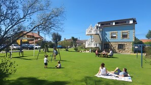 A grassy outdoor area with a swing set, picnic table, and a building with a balcony. - Apartment 'El Burby II Surf & Family' (Somo)