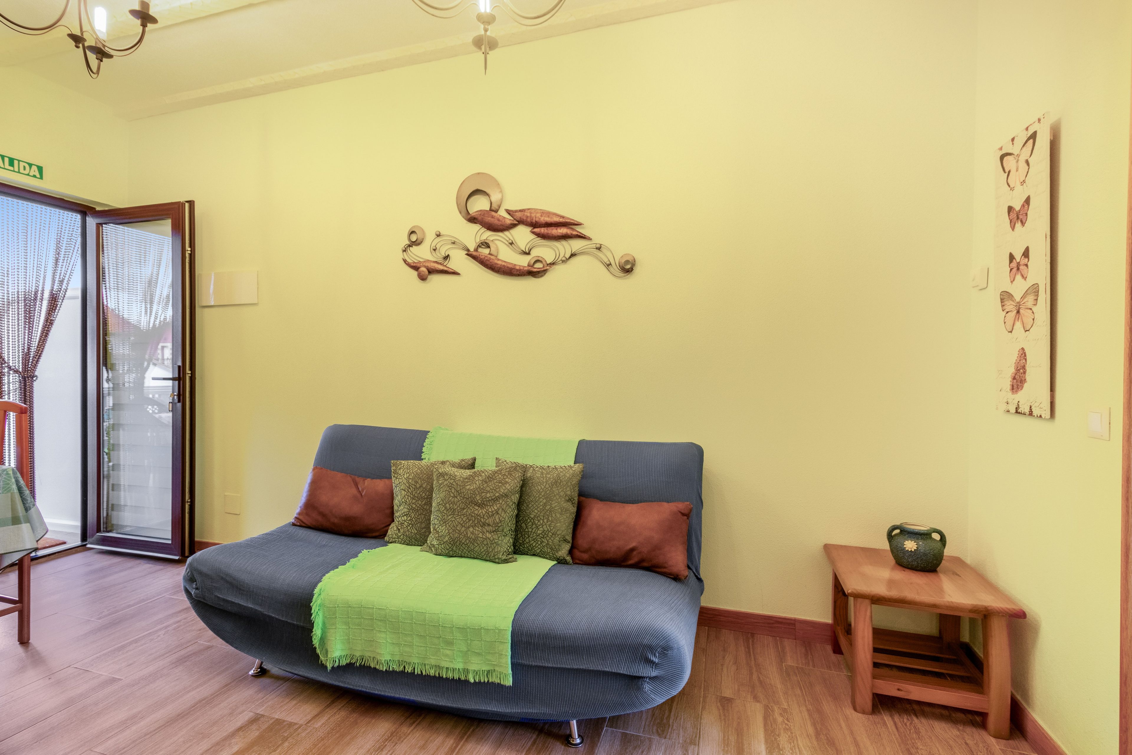 A room with a sofa, pillows, a small table, and a wall decoration.