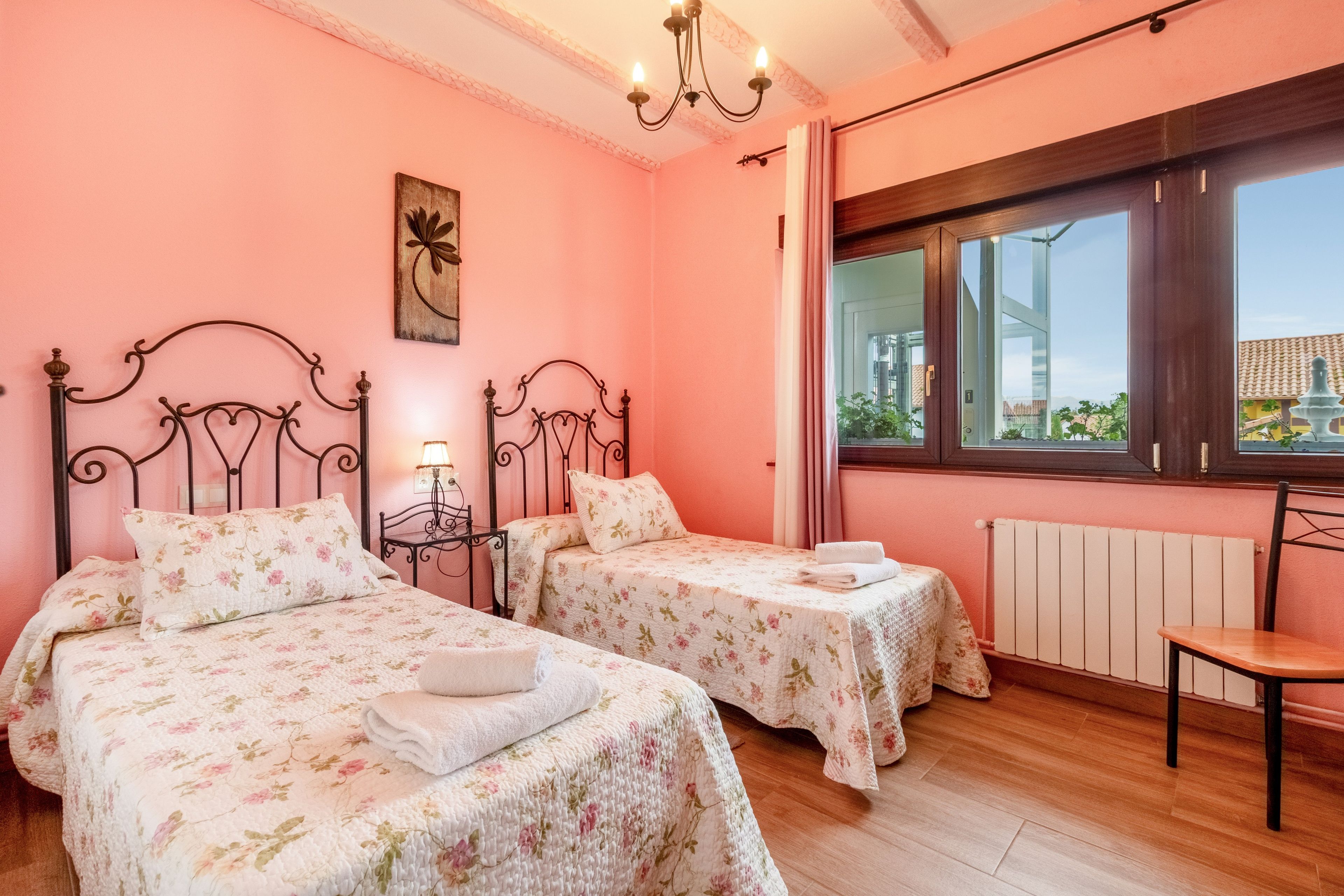 Une chambre avec deux lits, un lustre, une fenêtre donnant sur un beau paysage et un radiateur.