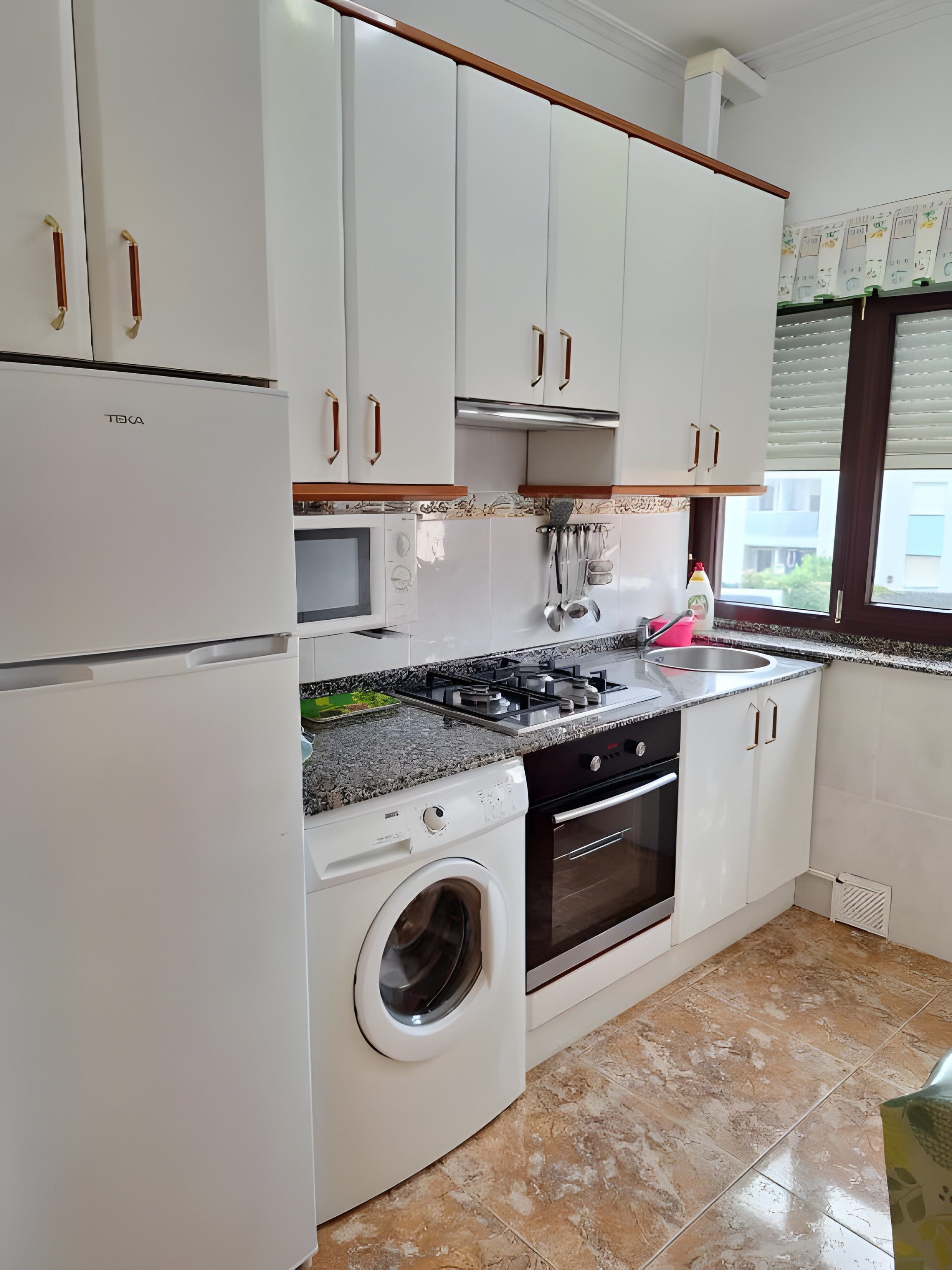 A kitchen with white cabinets, a built-in washing machine, a stove, and a window with blinds.