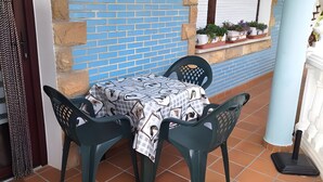 Eine Terrasse mit Tisch und Stühlen, eine blaue Ziegelwand und ein Fenster mit geschlossenen Rollläden.