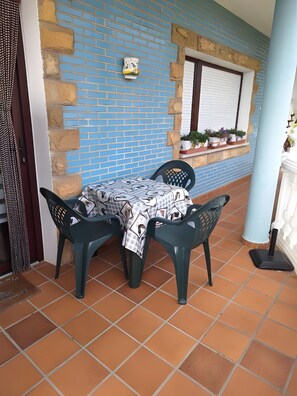 A patio with a table and chairs, a blue brick wall, and a window with closed shutters. - Apartment 'El Burby II Surf & Family' (Somo)