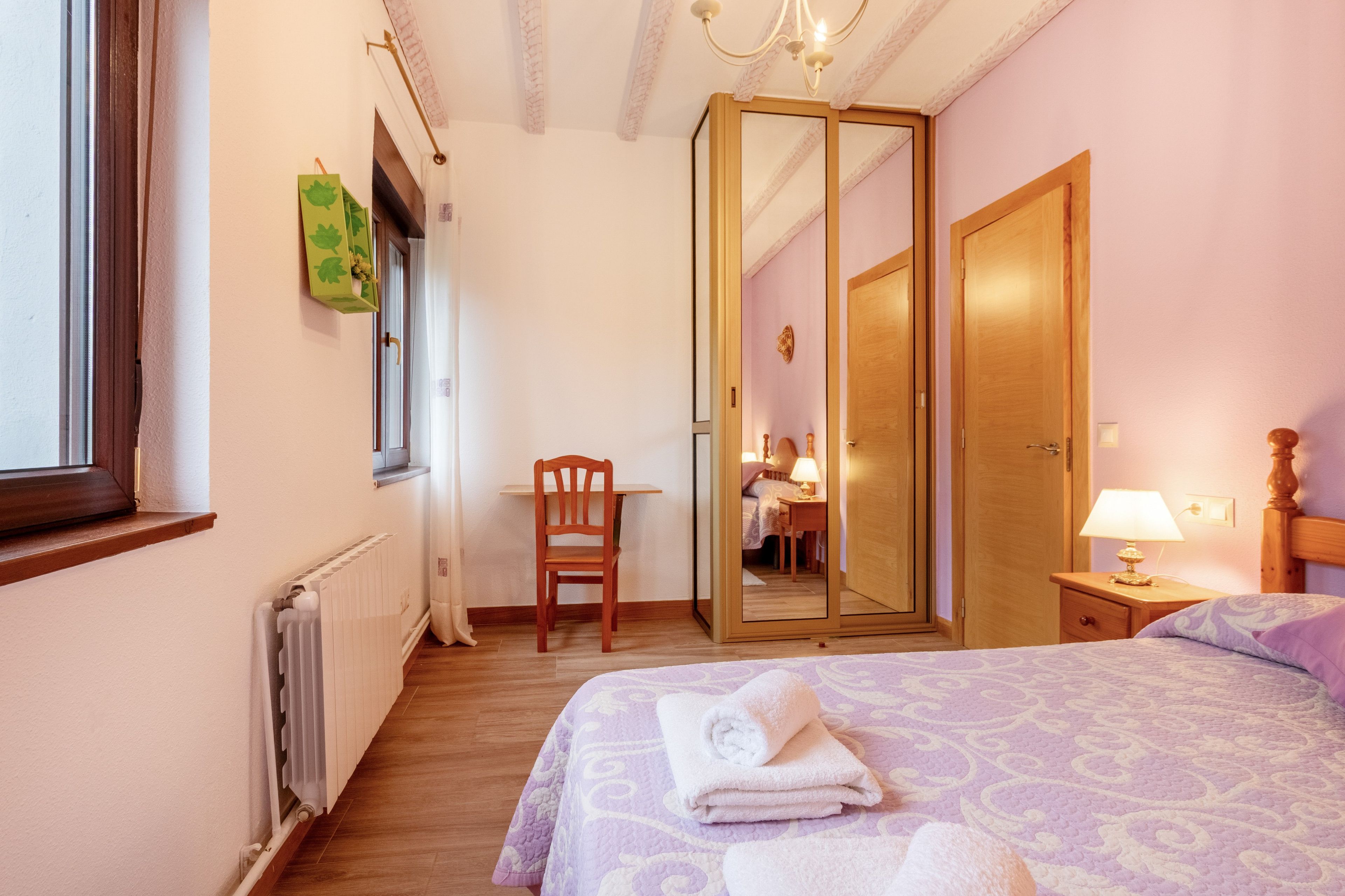 Ein Schlafzimmer mit einem Bett, einem Sessel, einem Spiegel, einer Heizung und einem Fenster.