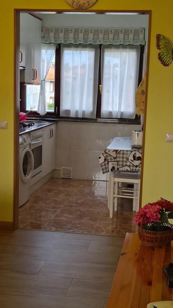 A kitchen with a washing machine, a dining table with chairs, and a window with curtains. - Apartment 'El Burby II Surf & Family' (Somo)