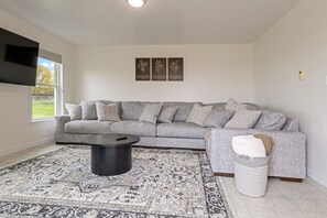 A living room with a grey sectional sofa, a round black coffee table, a patterned rug, and a white trash bin. - White Horse Overlook | Lancaster | Amish Country (Gap)