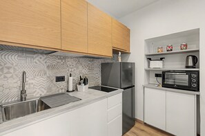 Een kleine keuken met een roestvrijstalen koelkast, een inbouwoven, een magnetron en een gootsteen met een moderne kraan.