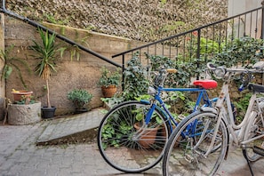 A blue bicycle parked on a cobblestone path with a metal railing and potted plants.