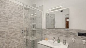 A modern bathroom with a glass-enclosed shower, a white sink with a mirror above, and a tiled wall. - Apartment 'Mimi' with Balcony, Wi-Fi and Air Conditioning (Taggia)