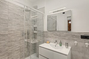 Een moderne badkamer met een douchecabine van glas, een wit wastafelmeubel met spiegel en een betegelde wand.