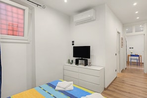 Un dormitorio con cama, televisor sobre un aparador, equipo de aire acondicionado y un pasillo que conduce a un comedor.