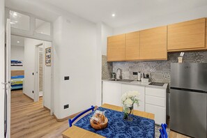 A compact kitchen with wooden cabinets, a stainless steel refrigerator, and a dining area with a table set for two.