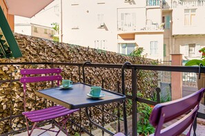 Un balcón con mesa y sillas, una pared decorada con hojas y vistas de los edificios circundantes.