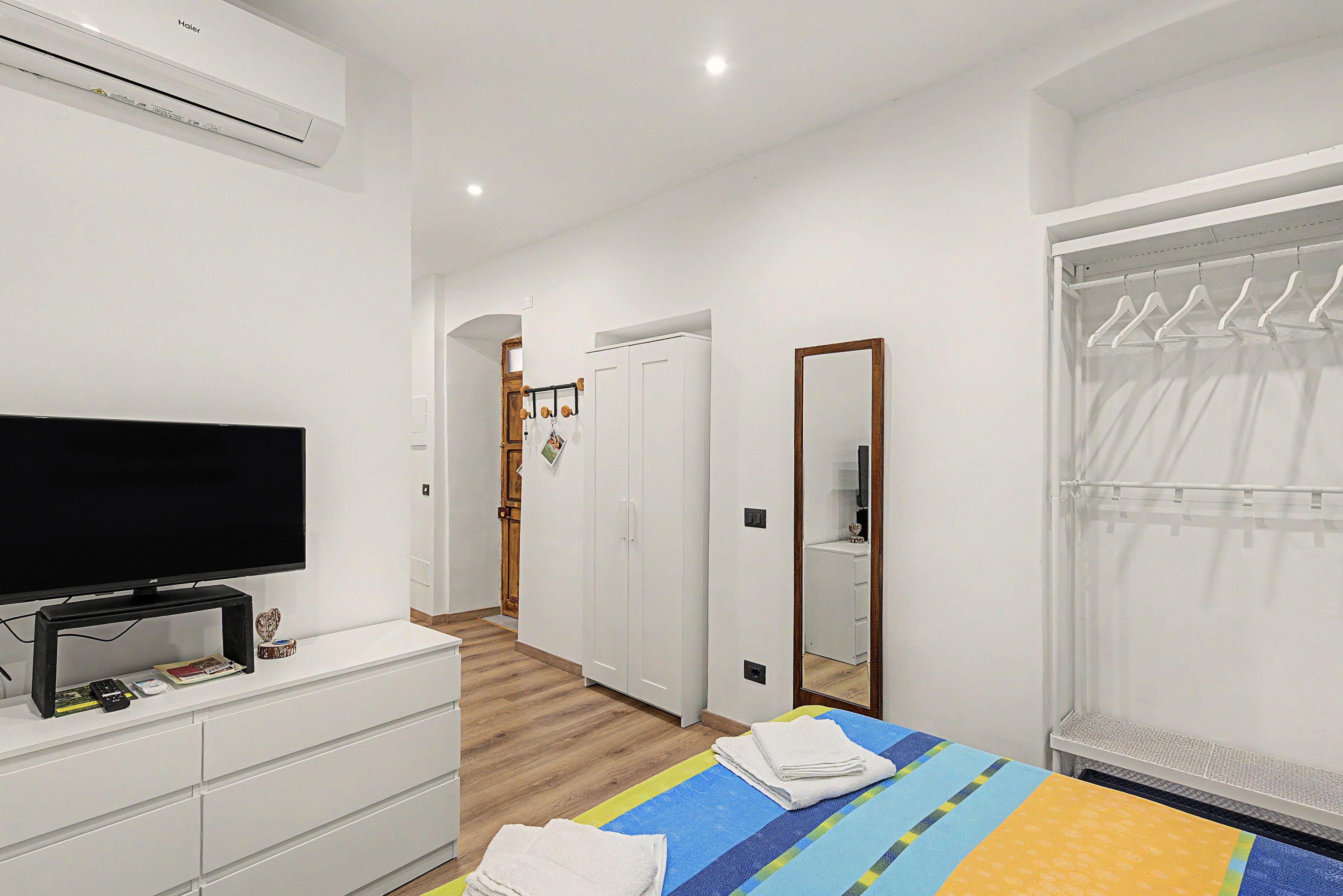 Een hotelkamer met een flatscreen televisie op een dressoir, een bed met gestreept beddengoed, een houten deur en een raam met gordijn.