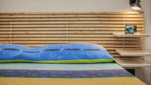 A bed with a blue and green patterned bedspread, a wooden slat headboard, a bedside table with a lamp, and a small shelf with a decorative item. - Apartment 'Mimi' with Balcony, Wi-Fi and Air Conditioning (Taggia)