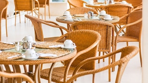 A series of wicker tables with chairs, each set with white cups and saucers, suggesting a dining or tea area. - Sunbay- Breakfast, hotel, WiFi, Beach Access (Bridgetown)