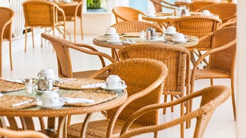 A series of wicker tables with chairs, each set with white cups and saucers, suggesting a dining or tea area.