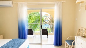 A hotel room with a bed, a dresser, a chair, and a balcony with curtains. - Sunbay- Breakfast, hotel, WiFi, Beach Access (Bridgetown)
