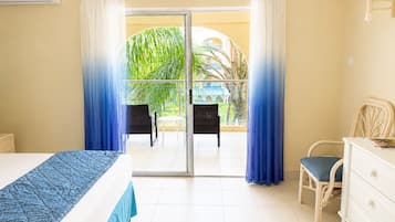 A hotel room with a bed, a dresser, a chair, and a balcony with curtains.