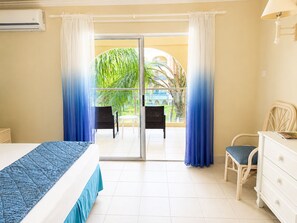 A hotel room with a bed, a dresser, a chair, and a balcony with curtains. - Sunbay- Breakfast, hotel, WiFi, Beach Access (Bridgetown)