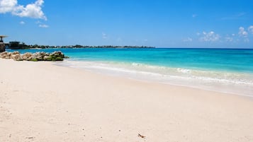 A beach with clear turquoise water, a sandy shore, and a distant shoreline with buildings.