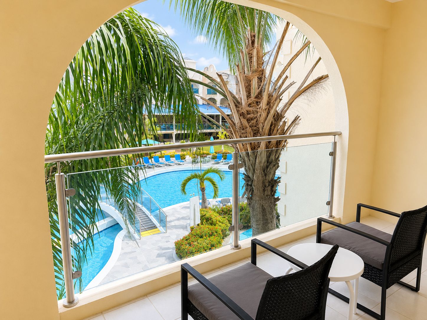 A balcony with a view of a swimming pool, palm trees, and a building in the background.