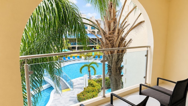 A balcony with a view of a swimming pool, palm trees, and a building in the background. - Sunbay- Breakfast, hotel, WiFi, Beach Access (Bridgetown)