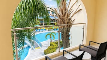 A balcony with a view of a swimming pool, palm trees, and a building in the background.