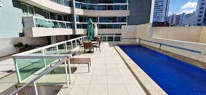 A rooftop pool area with a glass balustrade, lounge chairs, and a green umbrella. - COARM0113 - Cond The Place Beach Aparts (Salvador)