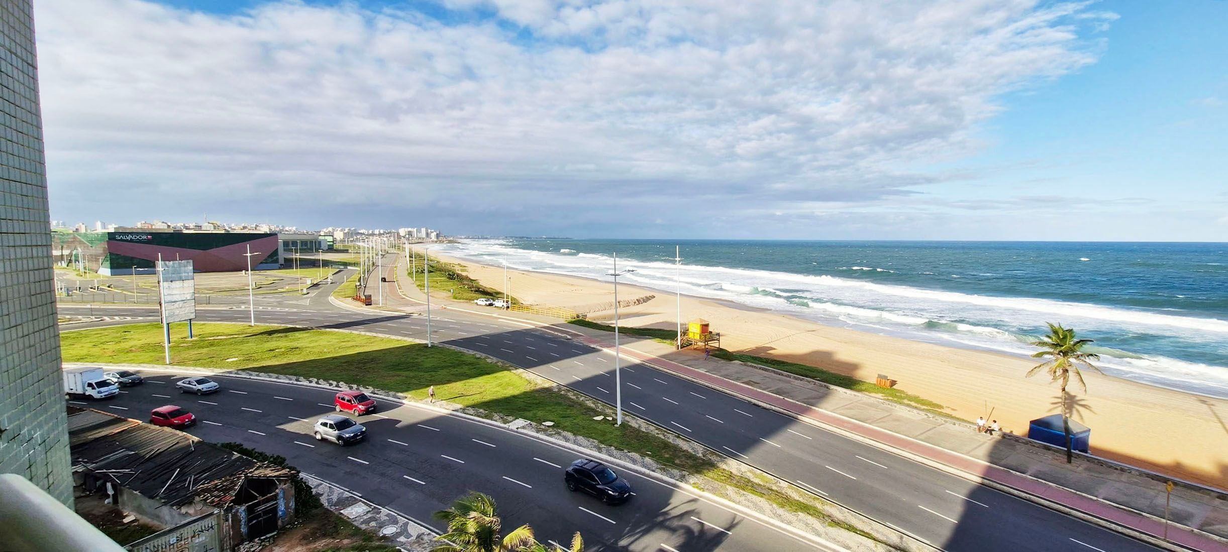 Une route côtière avec une plage et une vue sur l’océan, un espace de stationnement et un bâtiment portant l’inscription « SALVADOR ».