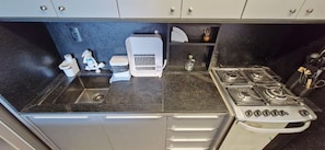 A compact kitchen with a gas stove, a sink, and a small countertop area. - COARM0113 - Cond The Place Beach Aparts (Salvador)