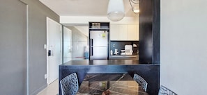 A modern kitchen with a dark countertop, white cabinets, and a refrigerator. - COARM0113 - Cond The Place Beach Aparts (Salvador)
