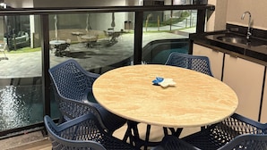 A modern outdoor dining area with a round table and chairs, a view of a swimming pool, and a glimpse of a building in the background. - Feet in the sand in Carneiros - Nomar (Tamandaré)