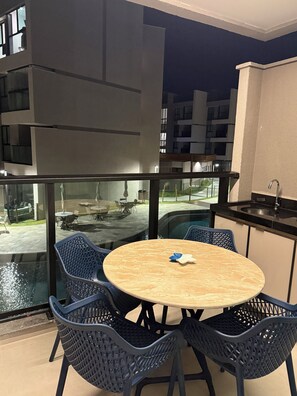 Ein moderner Essbereich im Freien mit einem runden Tisch und Stühlen, Blick auf einen Swimmingpool und ein Ausblick auf ein Gebäude im Hintergrund.