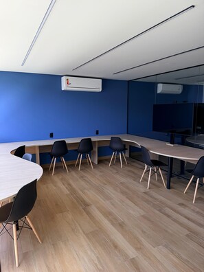 Ein Konferenzraum mit einem langen Tisch, schwarzen Stühlen und einer Klimaanlage an der Wand.