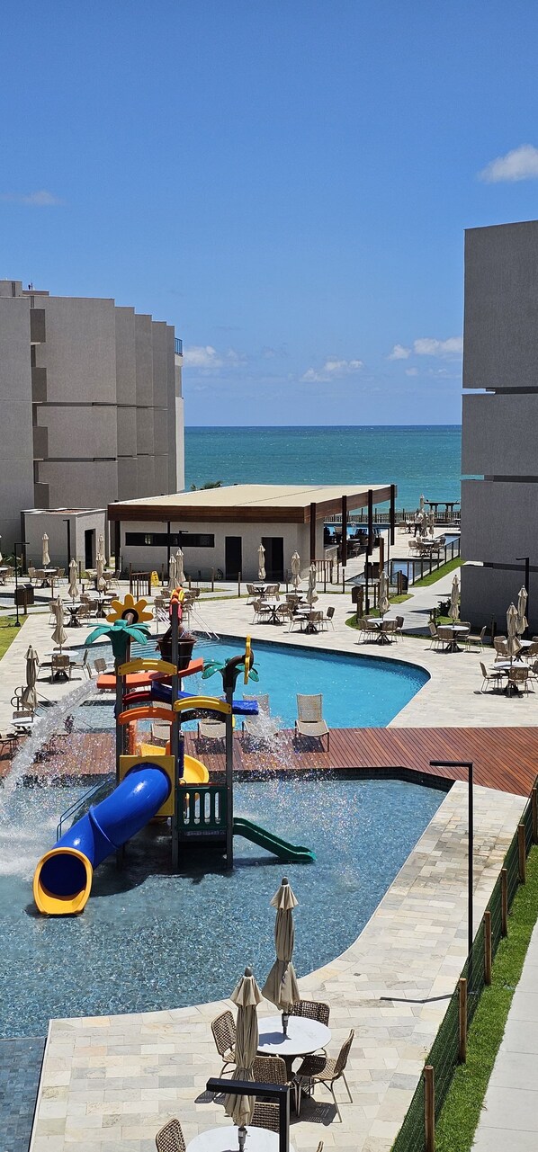 Ein Poolbereich eines Resorts mit Rutsche, Liegestühlen und Blick aufs Meer.