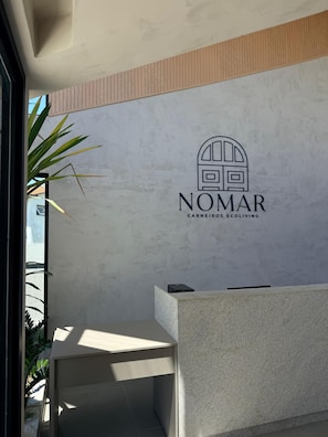 Ein Empfangsbereich mit dem Logo von 'NOMAR CARNEIROS ECOLIVING' vor einer strukturierten Wand.
