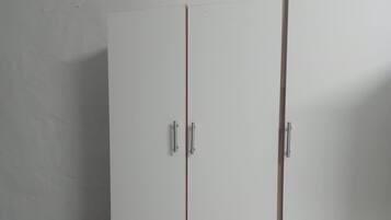 A white wardrobe with two doors and a small black stool.