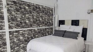 A bedroom with a stone wall, a bed with white bedding, and a small bedside table. - Room-tranquil Forest Studio Retreat in W (Westville)