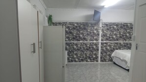 A compact room with a bed, a white wardrobe, a small refrigerator, and a stone-patterned wall. - Room-tranquil Forest Studio Retreat in W (Westville)