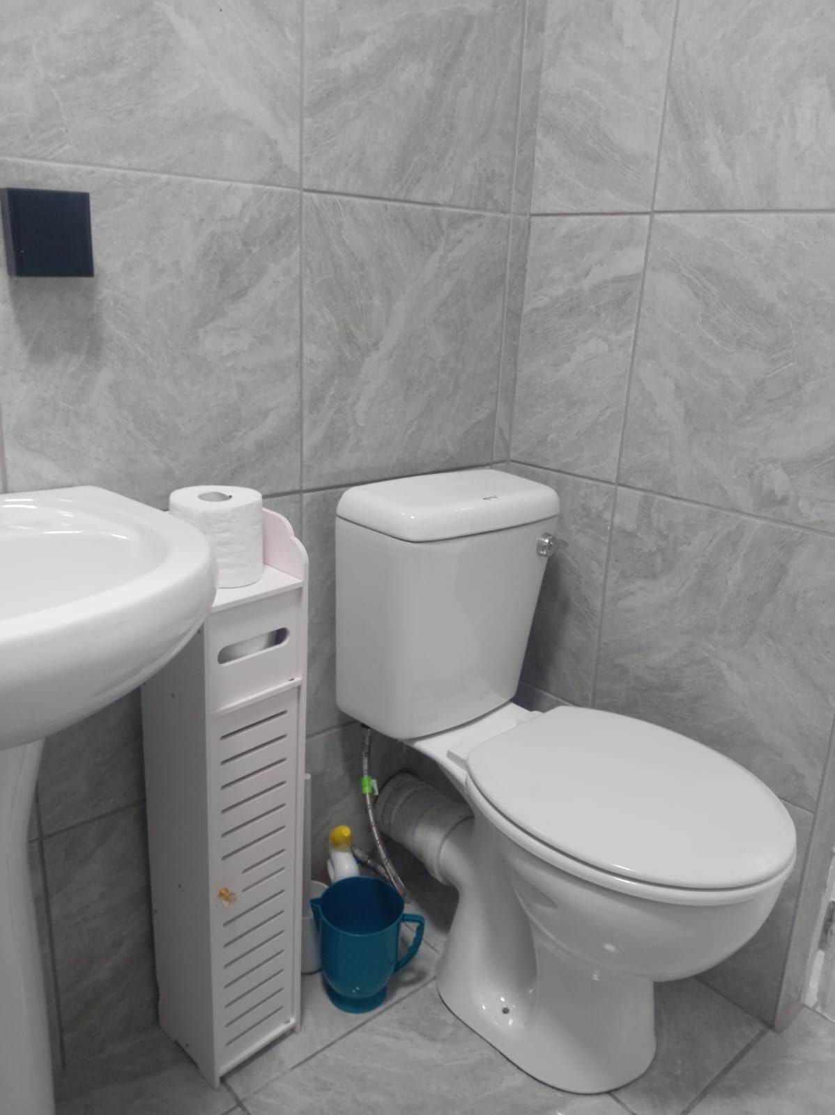 A bathroom with a toilet, sink, and a blue bucket.