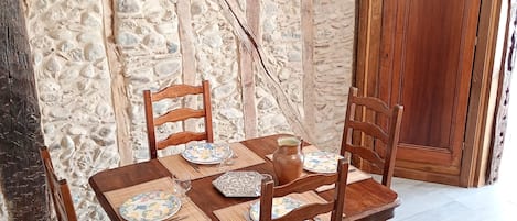 A wooden dining table set with plates, a pitcher, and chairs in a room with stone walls and a wooden cabinet.