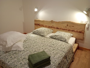 Un letto con una testiera in legno, una coperta a motivi decorativi e due cuscini. Sul letto c'è un asciugamano verde.
