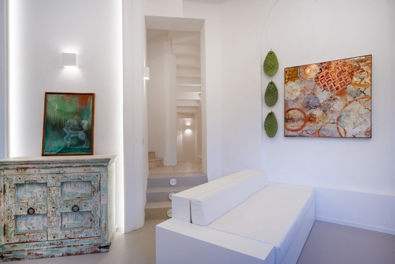 A modern interior with a staircase, a white sofa, and two paintings on the wall.