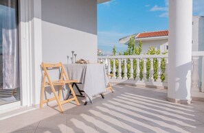 Ein Balkon mit Tisch und Stühlen, einem weißen Geländer und Blick auf ein Gebäude mit rotem Dach.