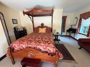 A four-poster bed with a red and gold patterned bedspread, a bedside table with a lamp, a small desk with a keyboard, and a chair with a red cushion. - A Serene Stay - Room #15 at The Inn At Herr Ridge (Gettysburg)