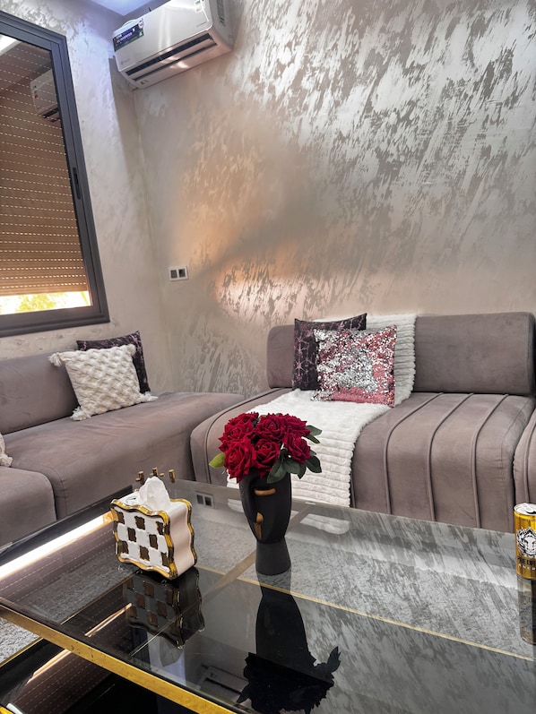 A modern living room with a sofa, a glass coffee table, and a vase with red roses.